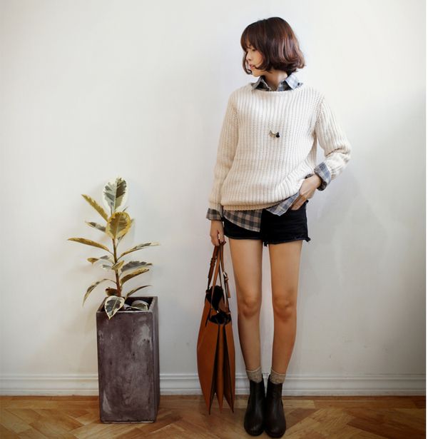 Woman in a chunky knit sweater and denim shorts holding a brown bag indoors