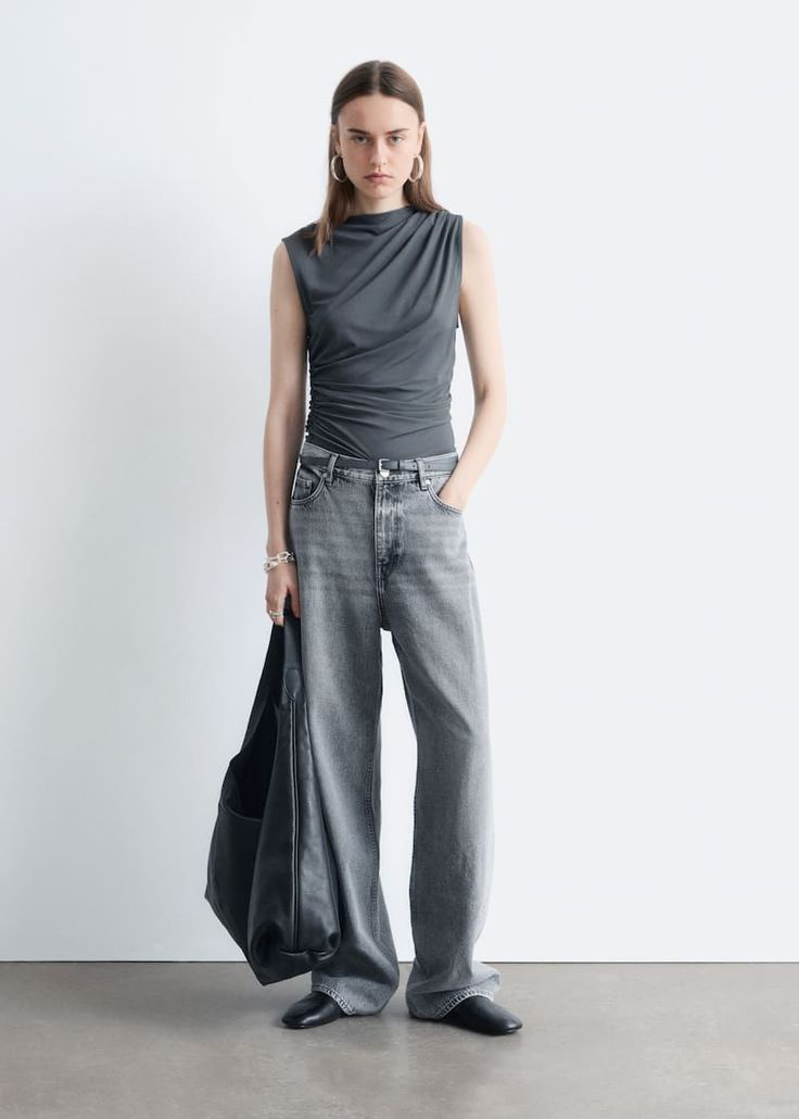 Woman in a gray sleeveless top and wide leg jeans holding a black bag