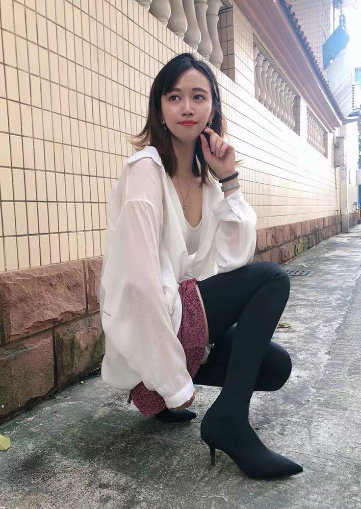 Woman in a white shirt and black leggings crouching on a street