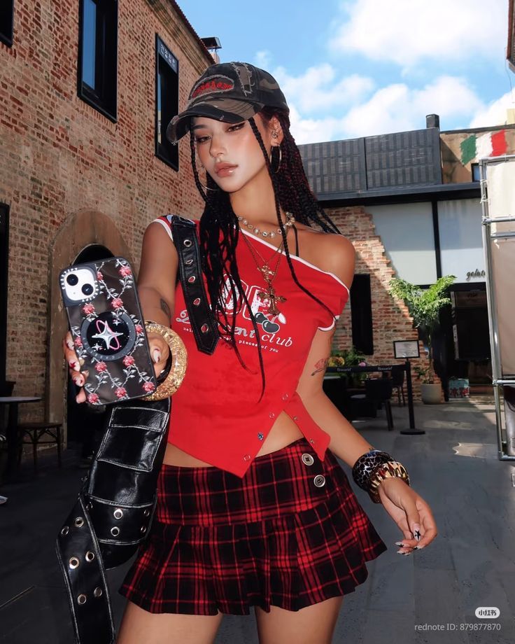 Woman in a red crop top and plaid skirt holding a phone outdoors