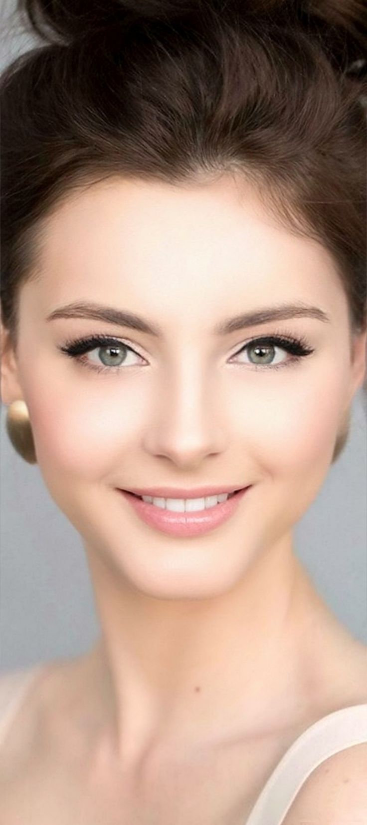 Woman with brown hair in an updo, smiling with green eyes and gold earrings