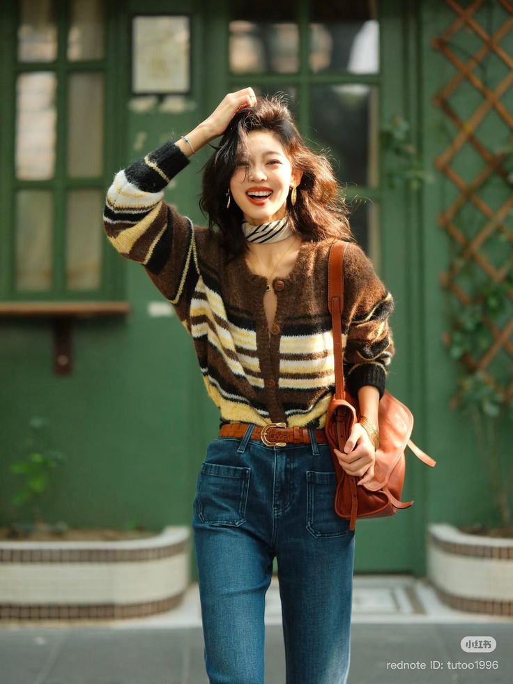 Woman in a striped cardigan and blue jeans smiling outdoors