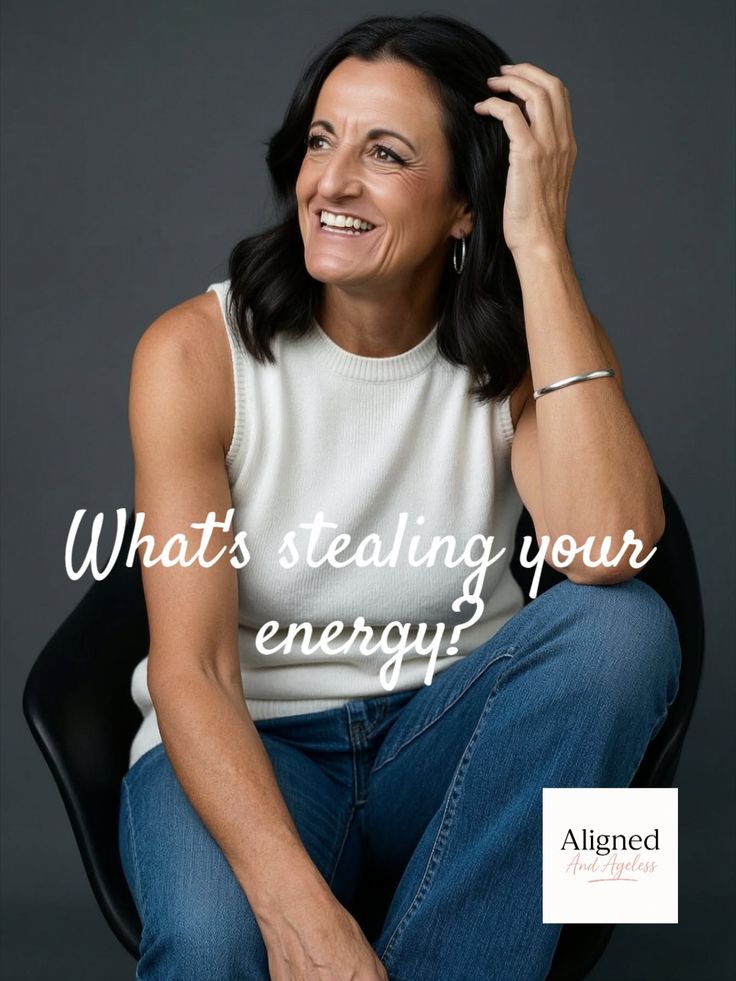Woman with dark hair wearing a white sleeveless top and blue jeans, smiling in a studio