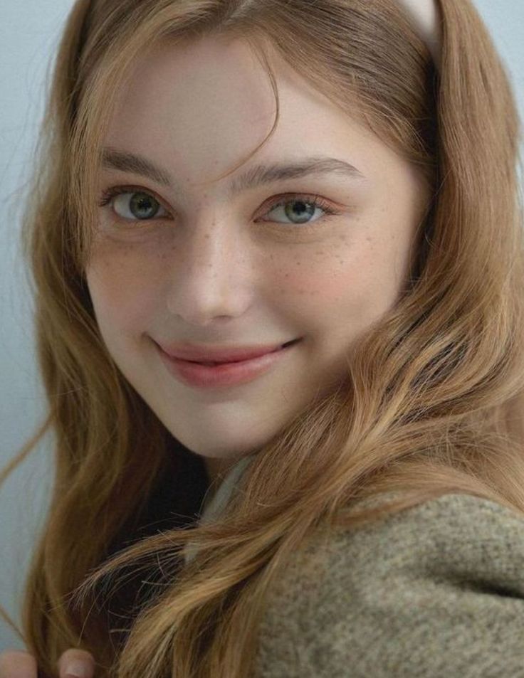 Young woman with long wavy hair and freckles smiling at the camera