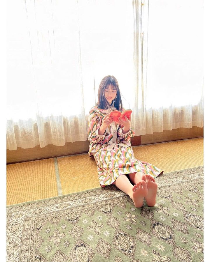 Woman in a colorful patterned dress sitting on a tatami mat and reading a book