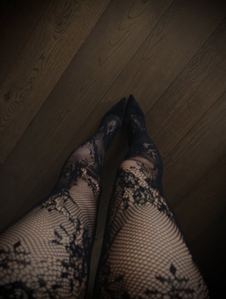 Legs in black lace stockings and high heels on a wooden floor