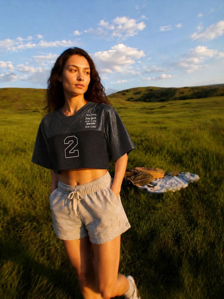 Woman in a crop top and shorts standing in a green field at golden hour