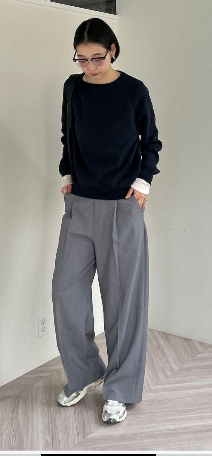 Woman with short hair and glasses wearing a black sweater and wide leg pants indoors