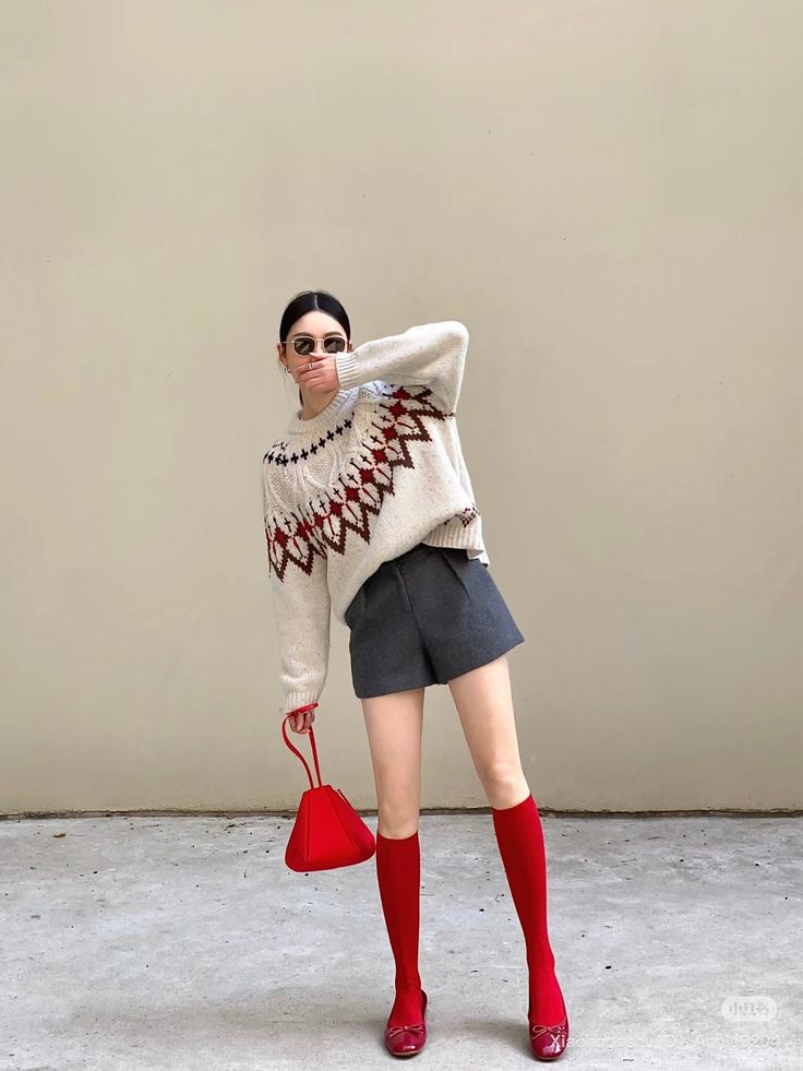 Woman in a fair isle sweater, gray shorts, and red accessories posing outdoors