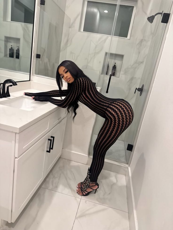 Woman in a black patterned jumpsuit and high heels posing in a bathroom