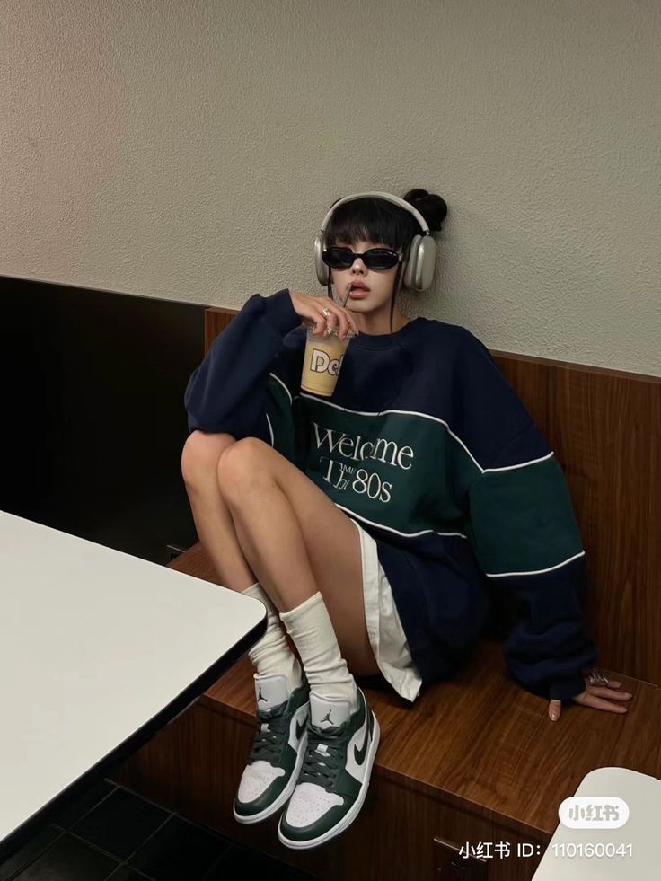 Person in an oversized sweatshirt, sunglasses, and headphones sitting indoors
