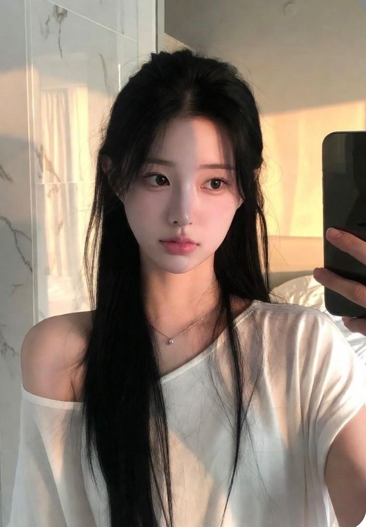 Woman with long black hair wearing a white off-shoulder top, taking a selfie