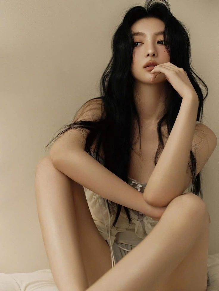 Woman with long black hair in a light top, sitting with exposed skin
