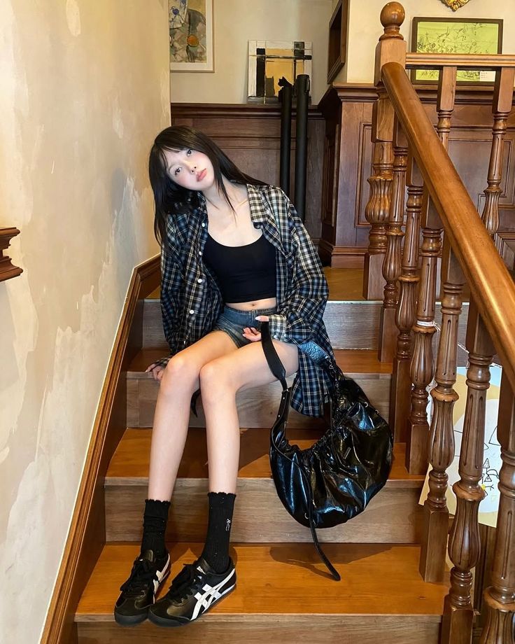 Woman with long black hair sitting on wooden stairs in a plaid shirt and crop top
