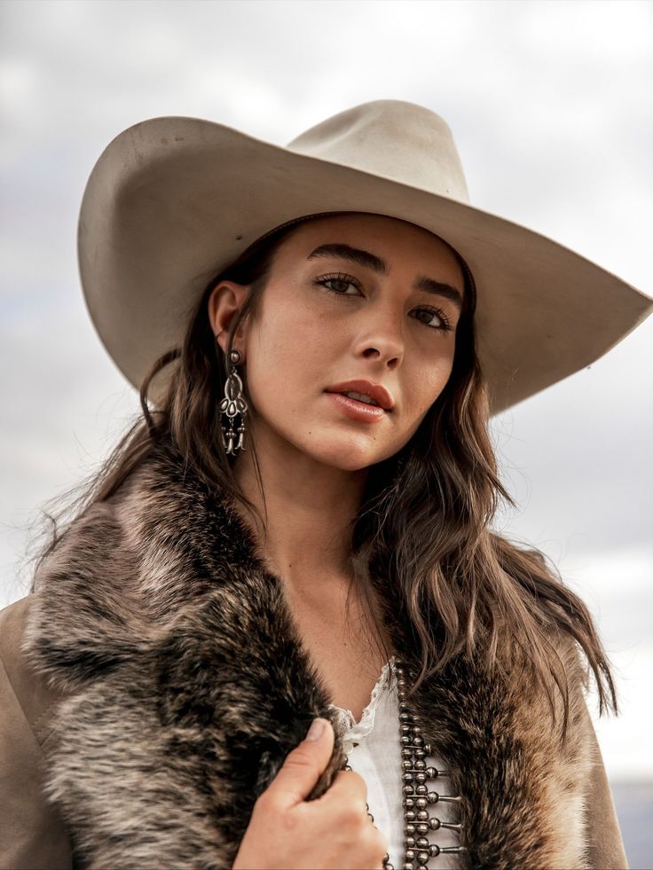 Woman in a cowboy hat and fur collar with silver earrings outdoors