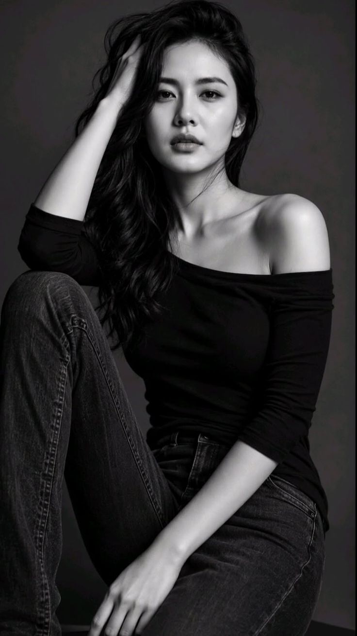 Woman with long hair wearing an off-shoulder top and jeans in a black and white portrait
