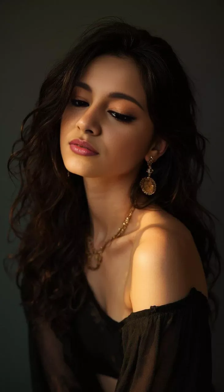 Woman with long wavy hair and gold jewelry in a black off-shoulder top