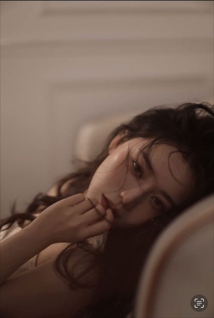 Woman with long dark hair in soft, warm lighting, with exposed skin