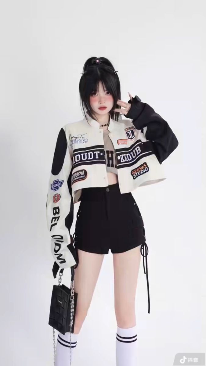 Woman in a racing jacket, crop top, and black shorts posing against a white background