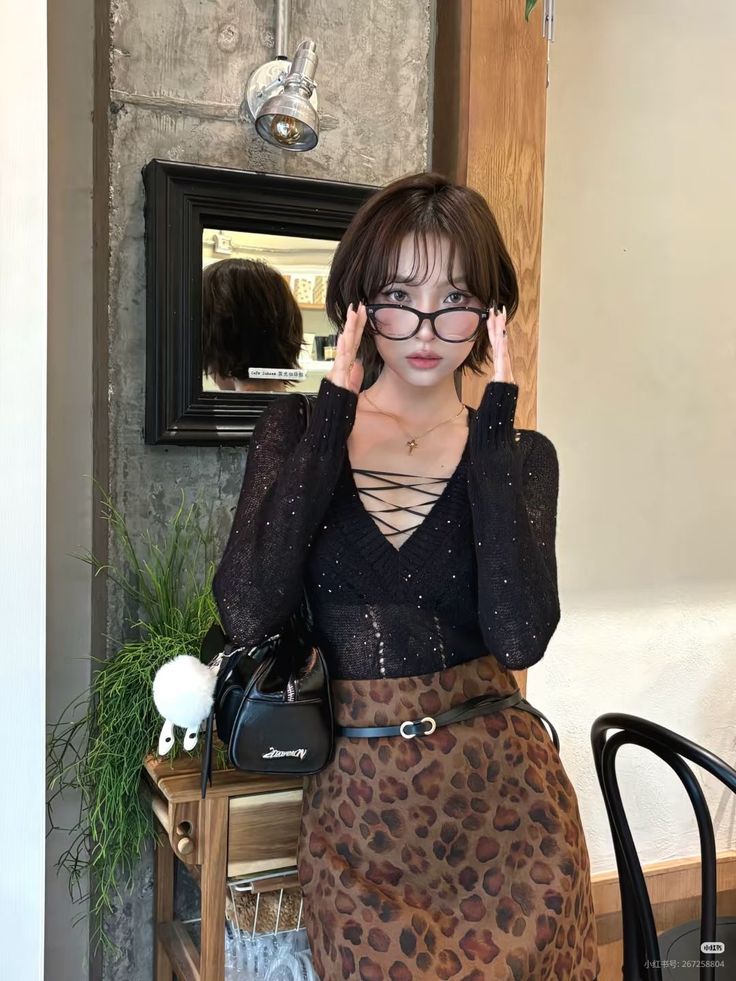 Woman with short hair and glasses wearing a lace-up top and leopard print skirt