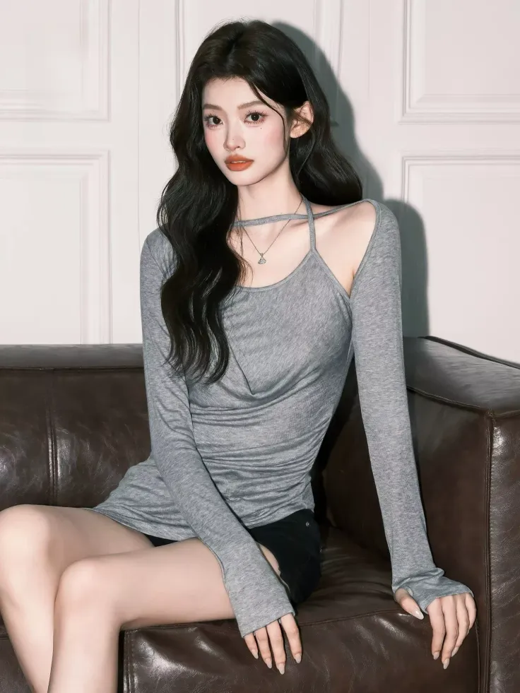 Woman with long dark hair wearing a gray top and black shorts, sitting on a couch