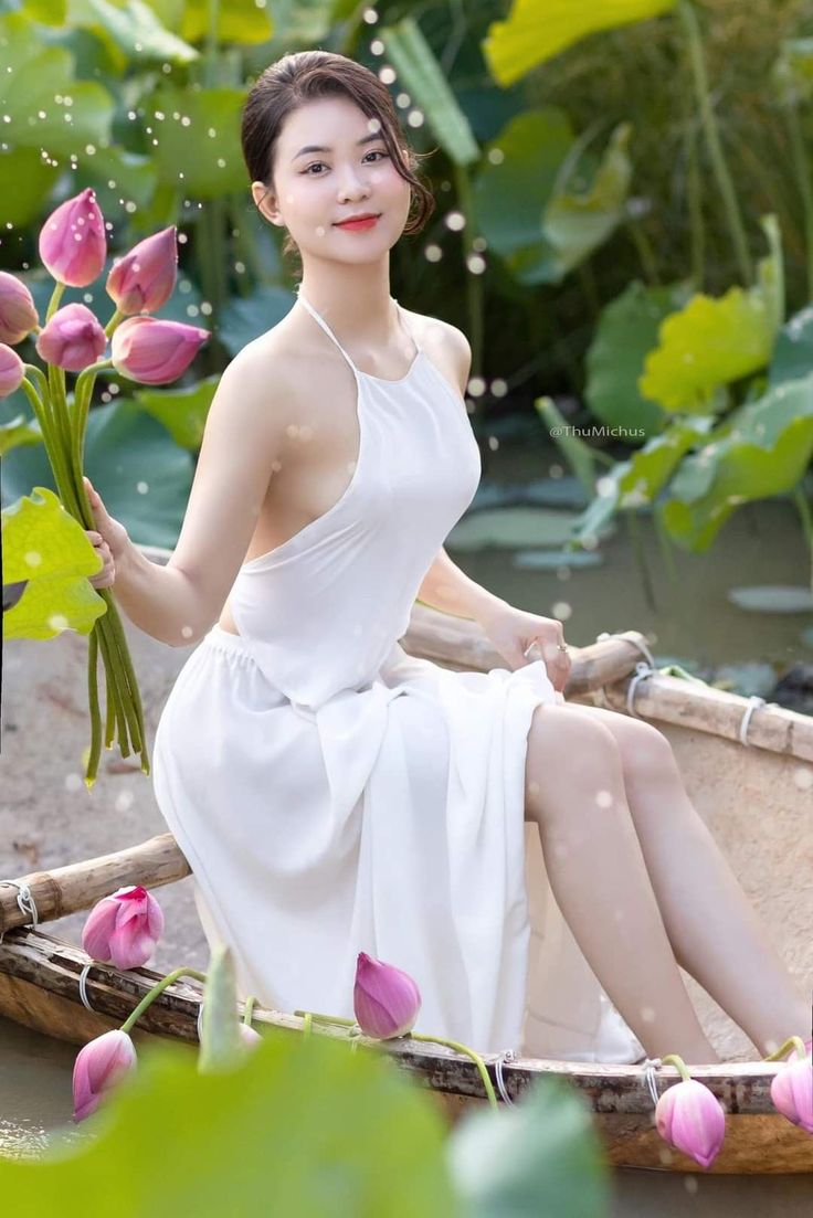 Woman in a white dress holding lotus flowers while sitting in a boat