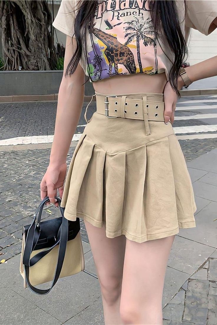 Woman in a crop top and pleated skirt holding a handbag on a street