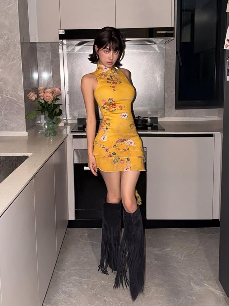 Woman in a yellow floral dress and black fringe boots standing in a kitchen