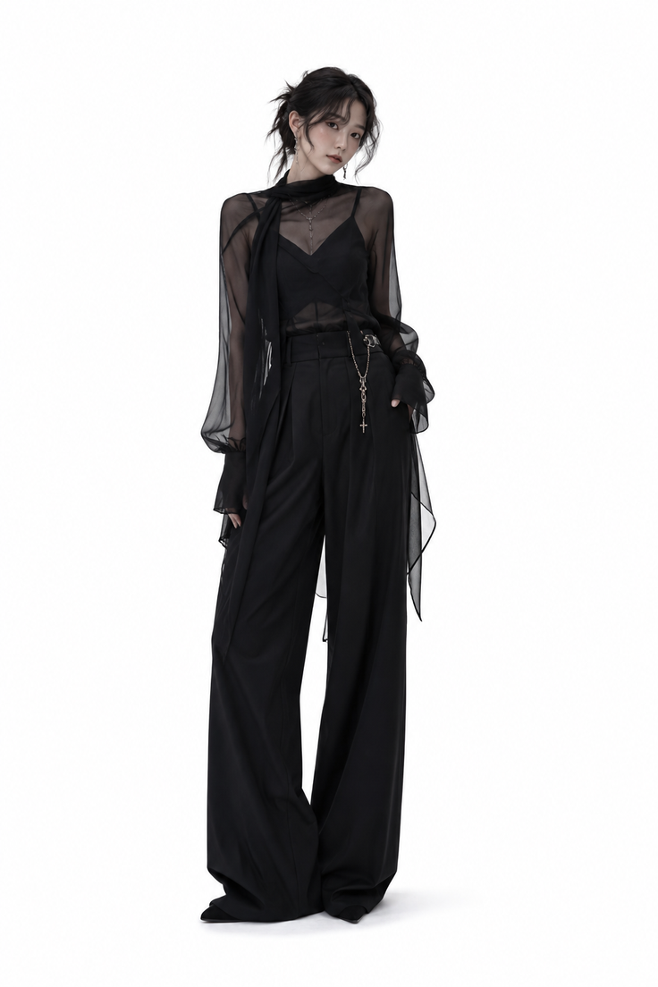 Woman in a black sheer top and wide-leg pants with a cross necklace