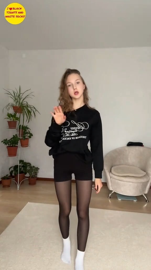 Young woman in black sweatshirt, black tights, and white socks indoors