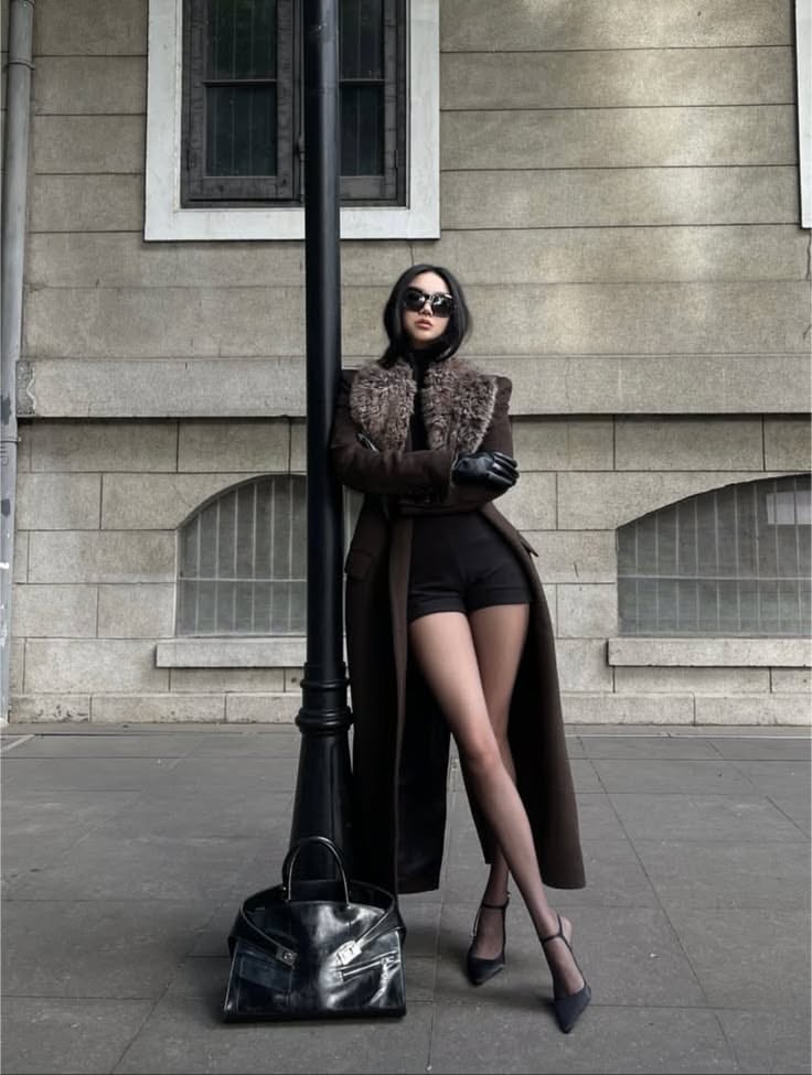 Woman in a long coat with a fur collar and black shorts on a street