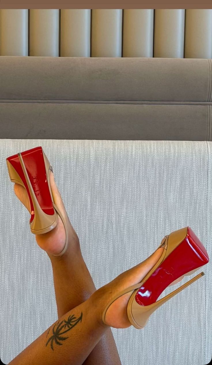 Legs crossed with nude high heels featuring red soles and a palm tree tattoo