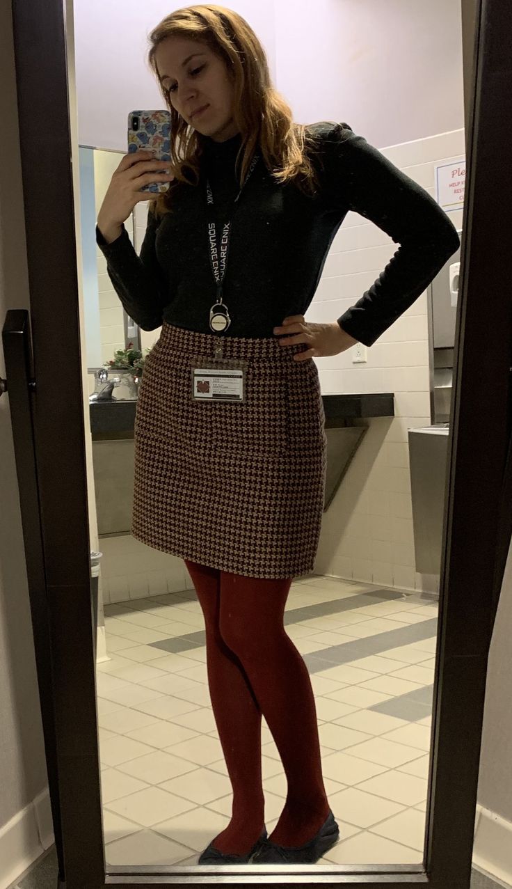 Woman in a black turtleneck, houndstooth skirt, and red tights taking a mirror selfie