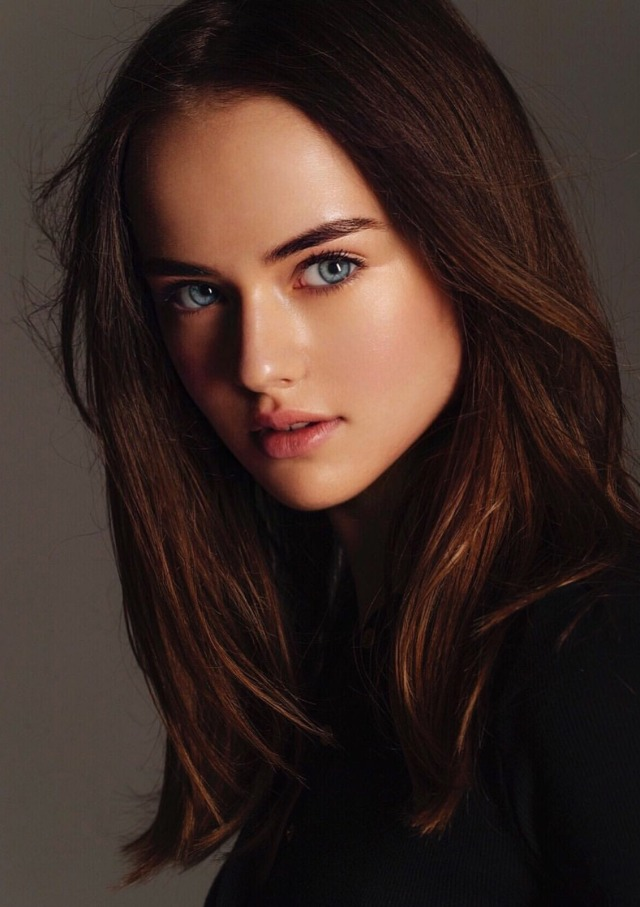 Close-up portrait of a woman with long brown hair and striking blue eyes