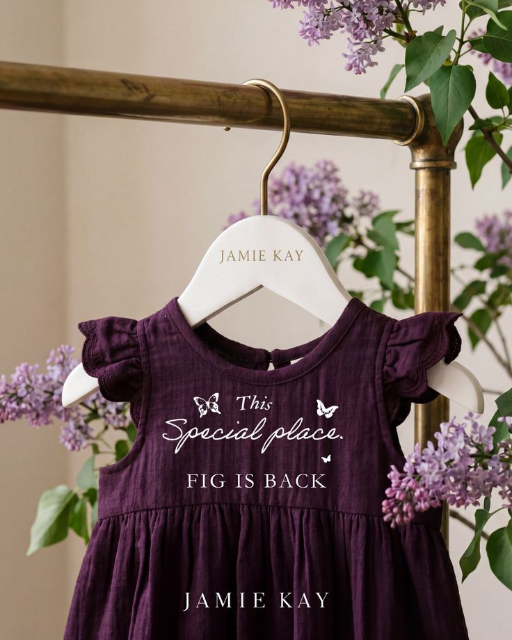 Purple baby dress with ruffle sleeves on a hanger surrounded by lilac flowers