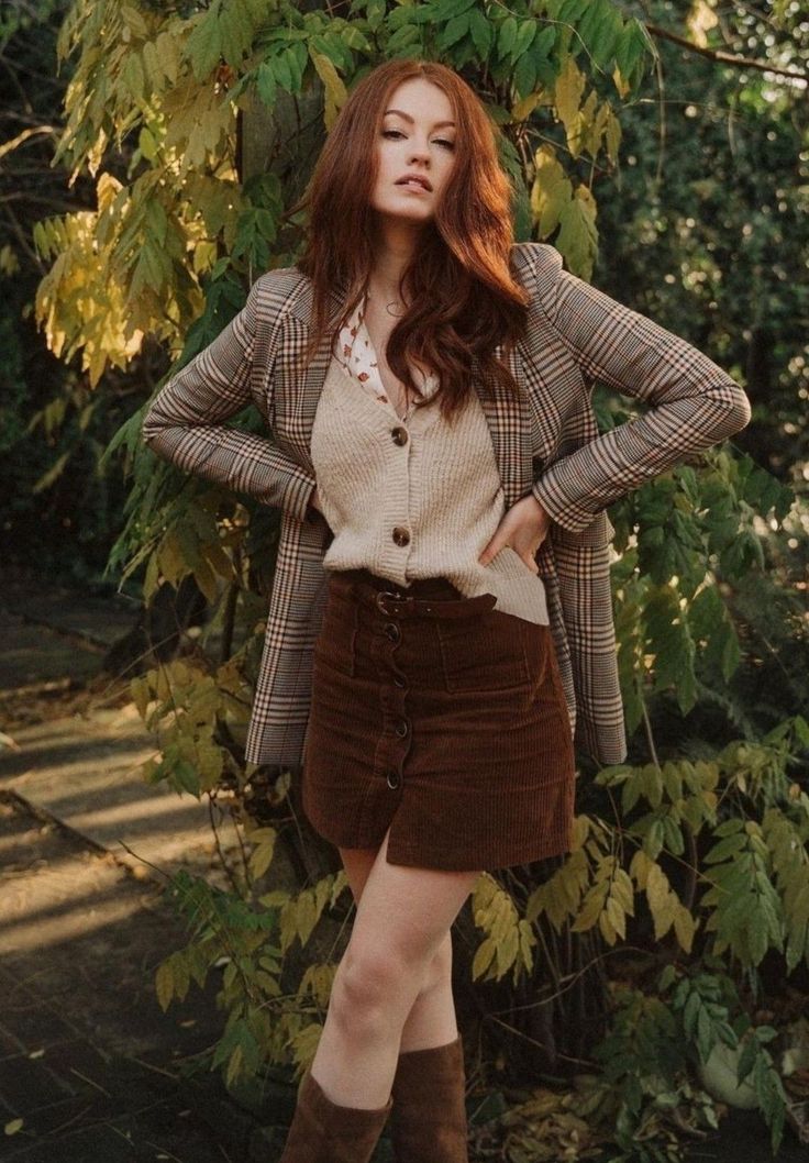 Woman with long red hair wearing a plaid blazer and corduroy skirt outdoors