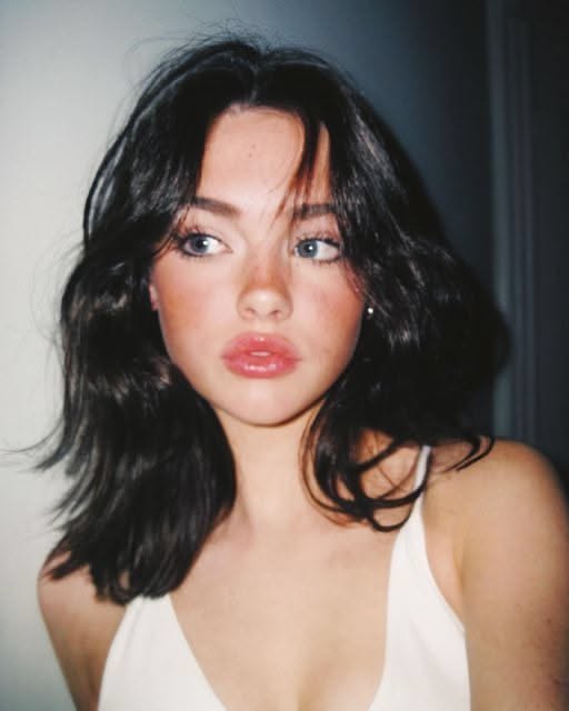 Woman with dark, medium-length hair and pink lips in a white top
