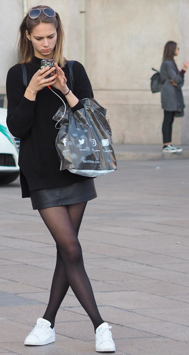 Woman in a black sweater and leather skirt looking at her phone on a street