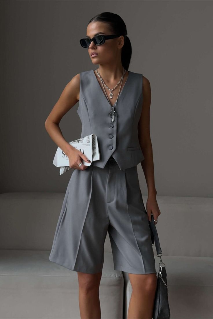 Woman in a gray vest and shorts holding a newspaper and bag