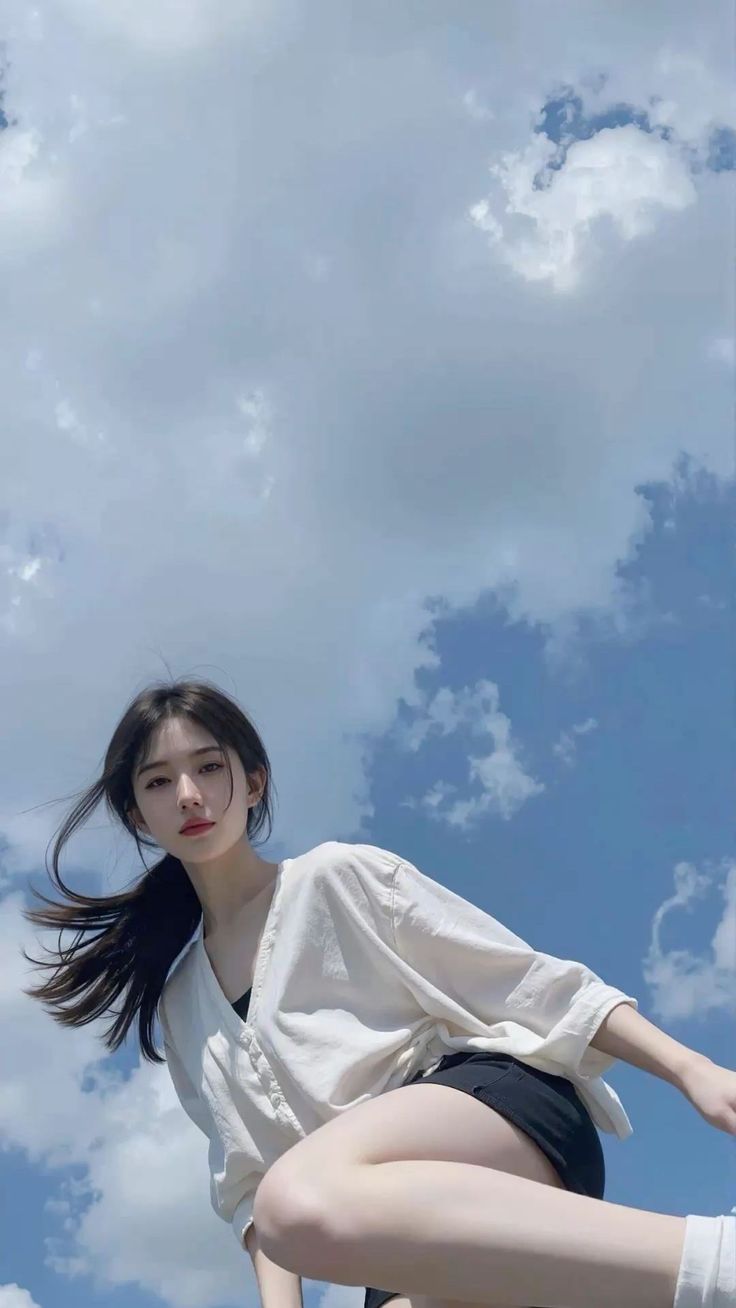 Woman in a white shirt and black shorts against a blue sky with clouds