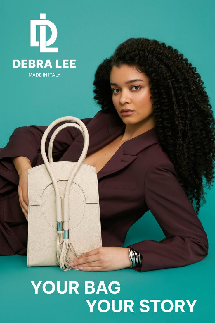 Woman with curly hair in a blazer holding a handbag against a teal background