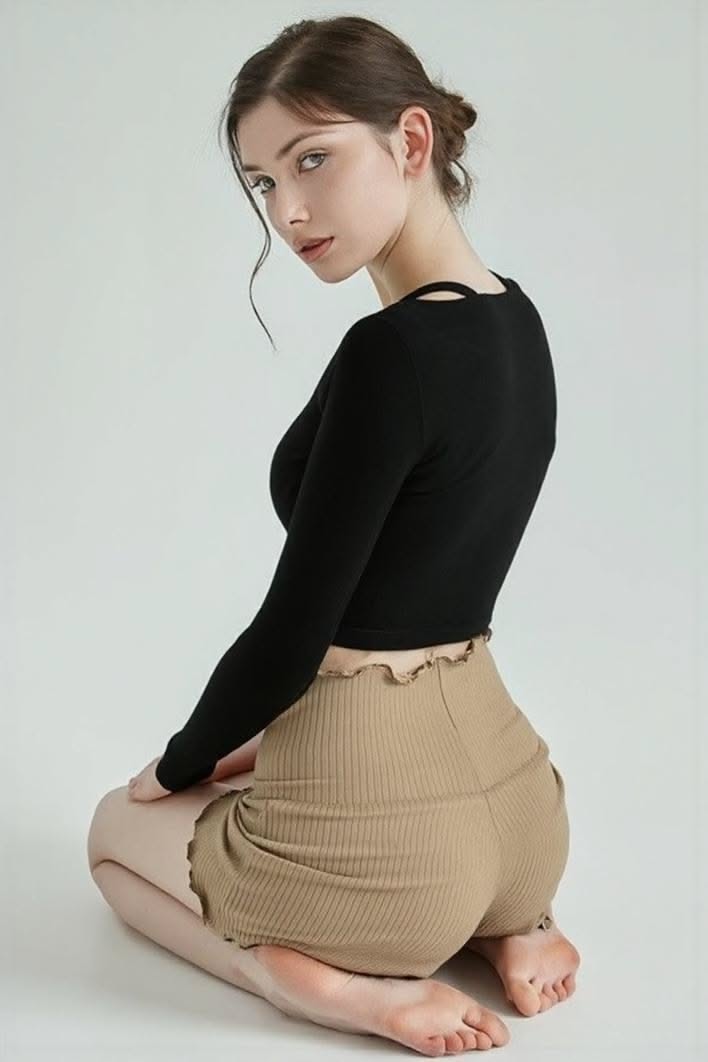 Woman in a black long-sleeve top and brown shorts kneeling in a studio