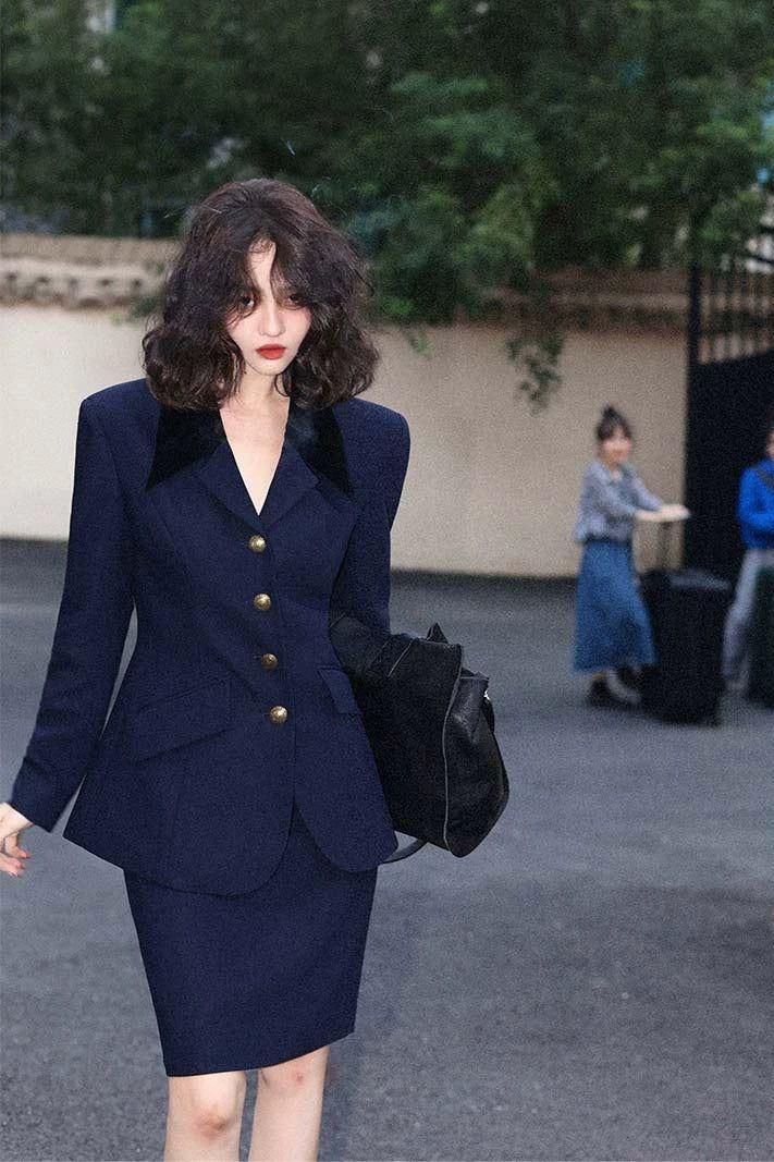 Woman in a navy blue suit with short wavy hair and red lipstick outdoors