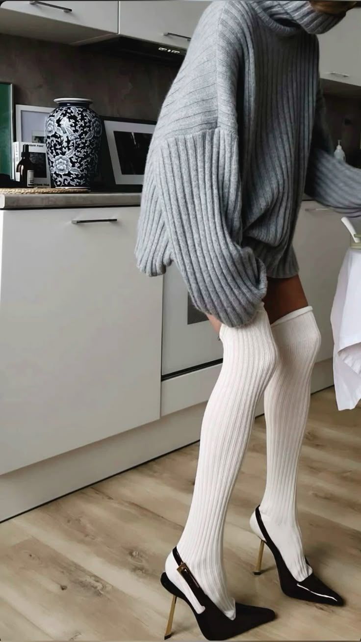 Woman in an oversized sweater, white thigh-high socks, and high heels in a kitchen