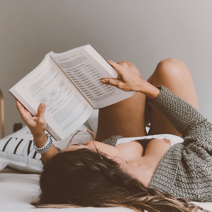 Woman with long hair reading a book while lying on a bed