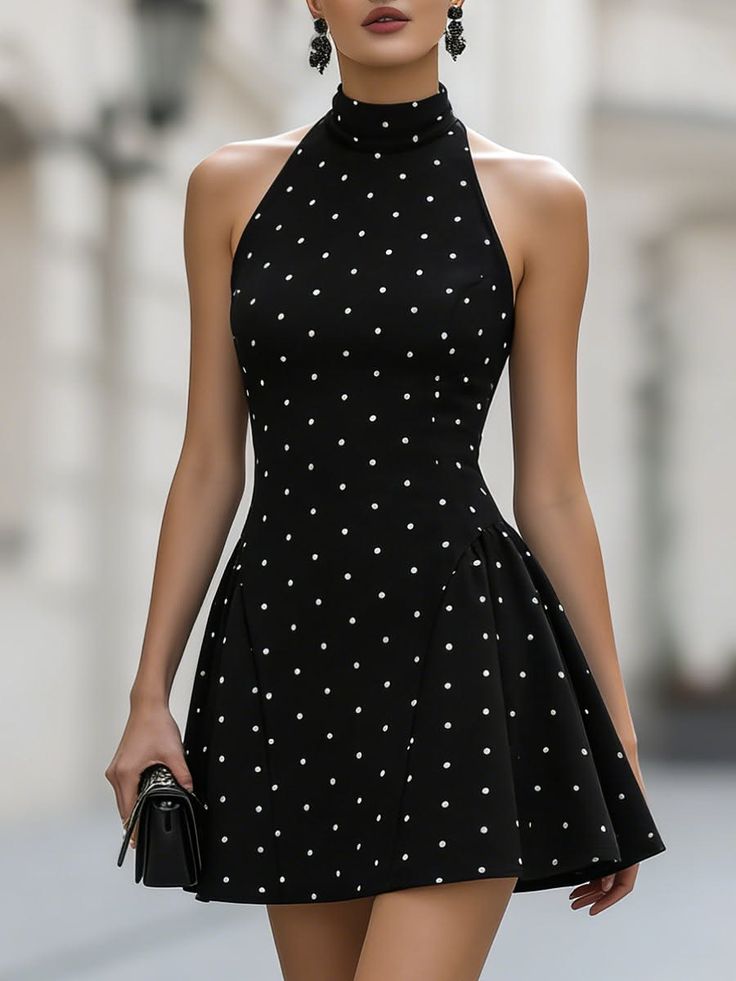 Woman in a black polka dot halter neck mini dress holding a handbag
