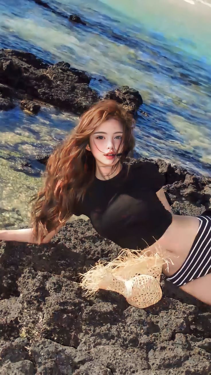 Woman with long hair in a black crop top and striped bikini bottom on a rocky beach