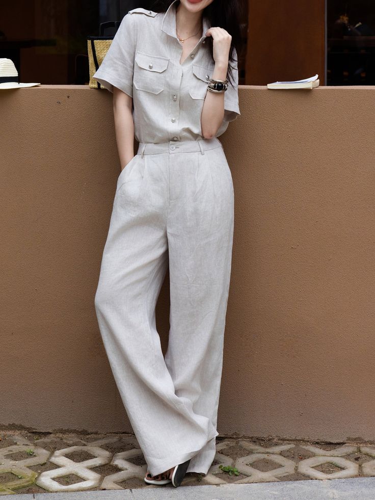Woman in a light-colored linen shirt and wide-leg pants leaning against a wall