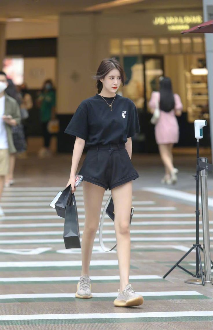 Woman in a black t-shirt and shorts walking on a street with shopping bags