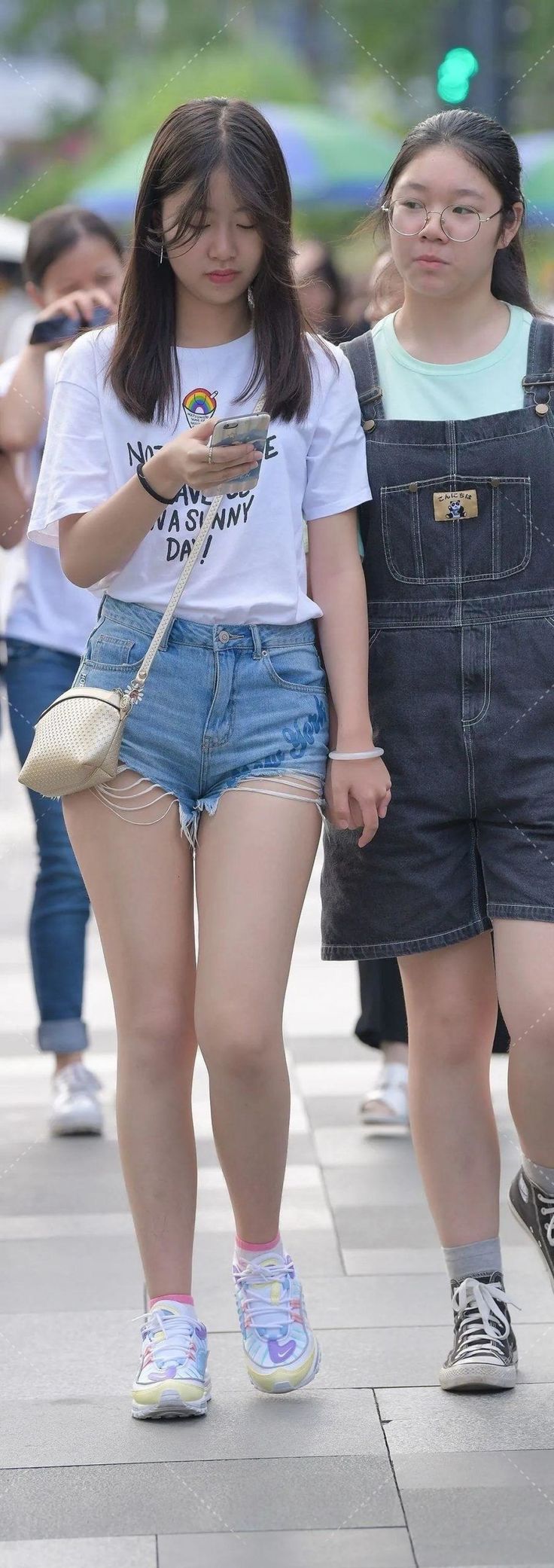 Two young women walking on a street, one in denim shorts and a white t-shirt